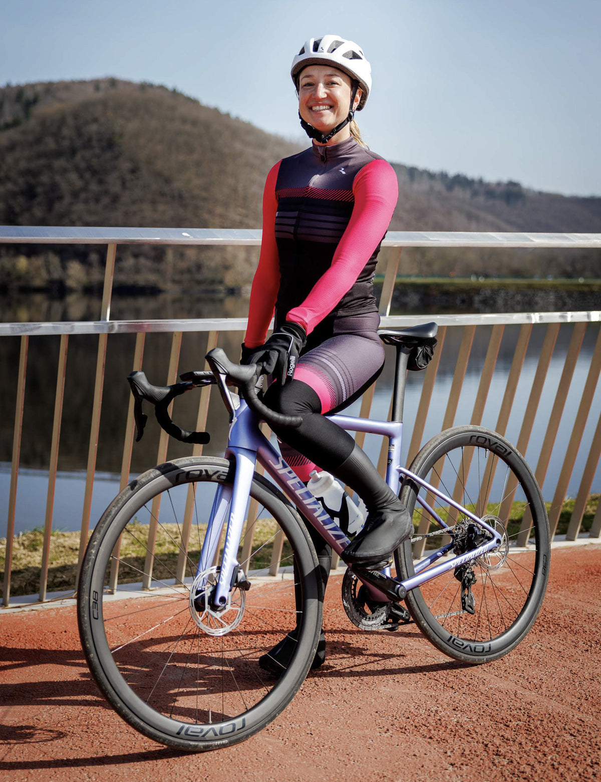 Vrouw in Rogelli Stryde bibtight dames in zwart, grijs en roze, zittend op een racefiets aan het water.