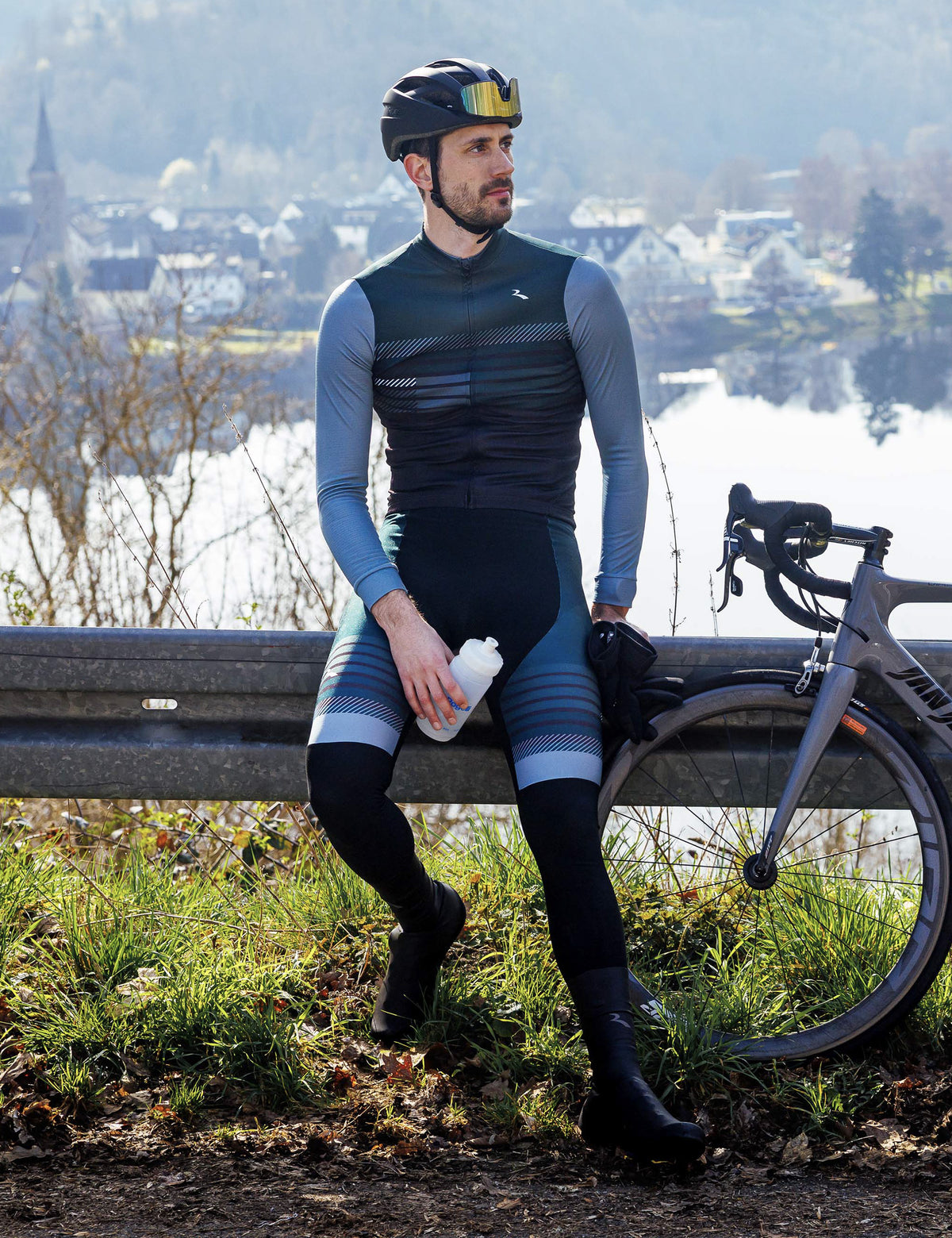 Man in Rogelli Stryde fietsshirt heren in zwart, grijs en blauw tijdens een rustmoment naast de racefiets.