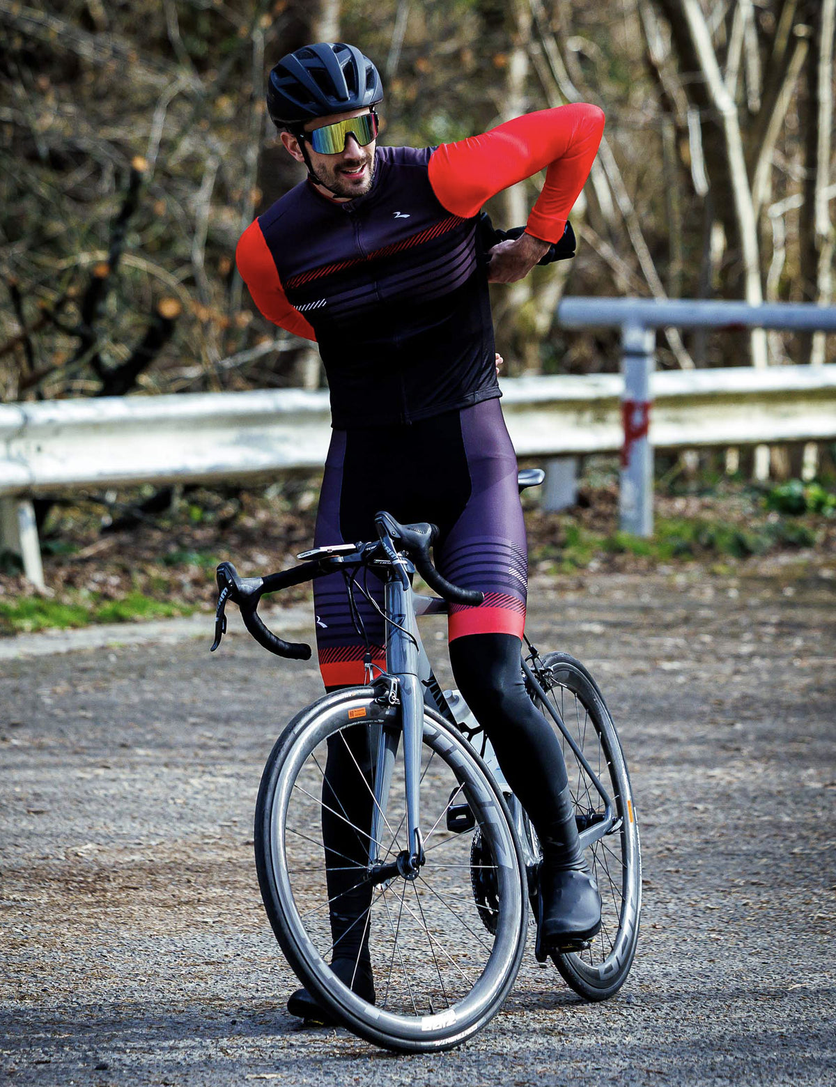 Man in zwart grijs rood Rogelli Stryde fietsshirt heren met lange mouwen naast zijn racefiets.