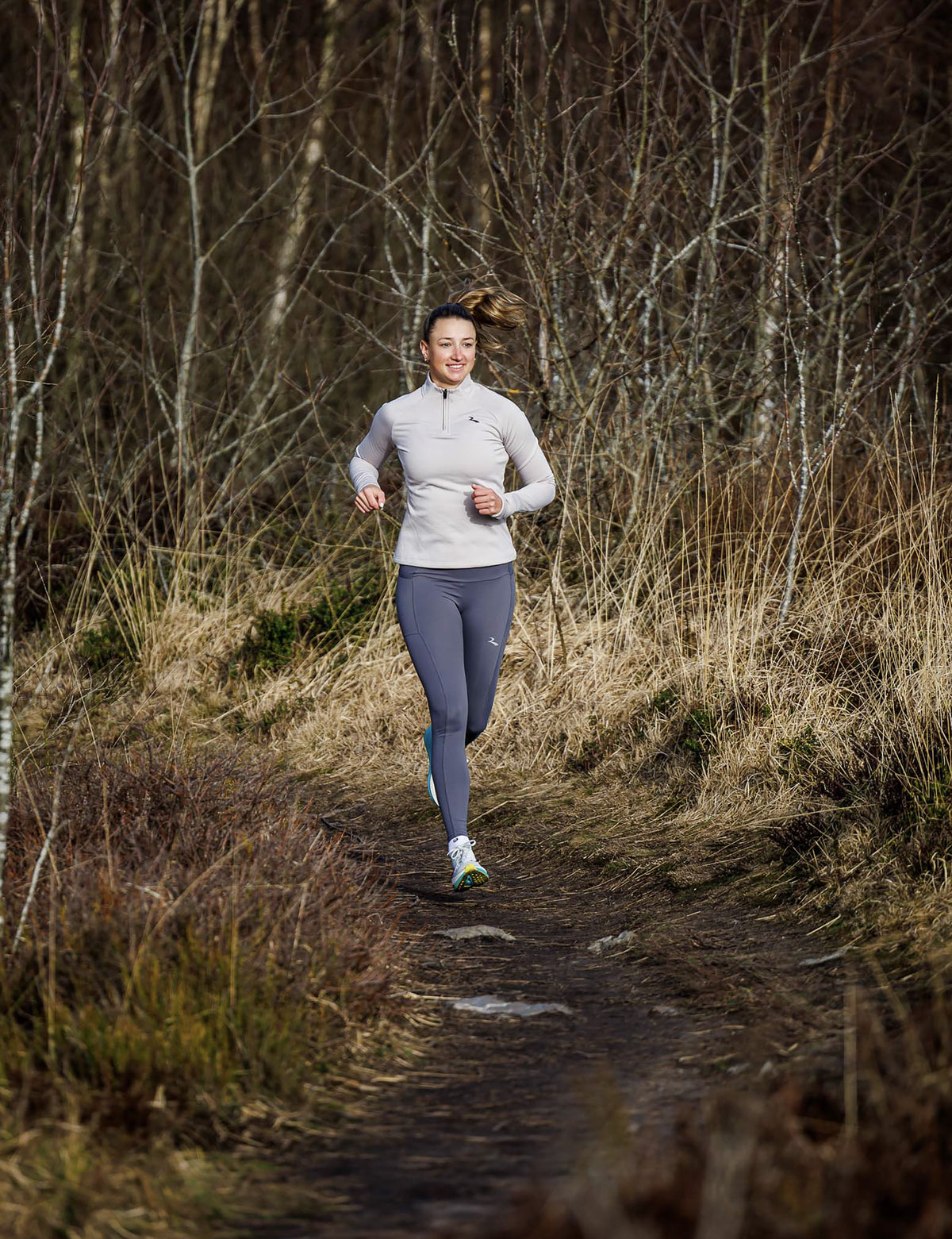 Vrouw in zandkleurige Rogelli Essential halfzip hardlooptop dames met lange mouwen en korte rits.
