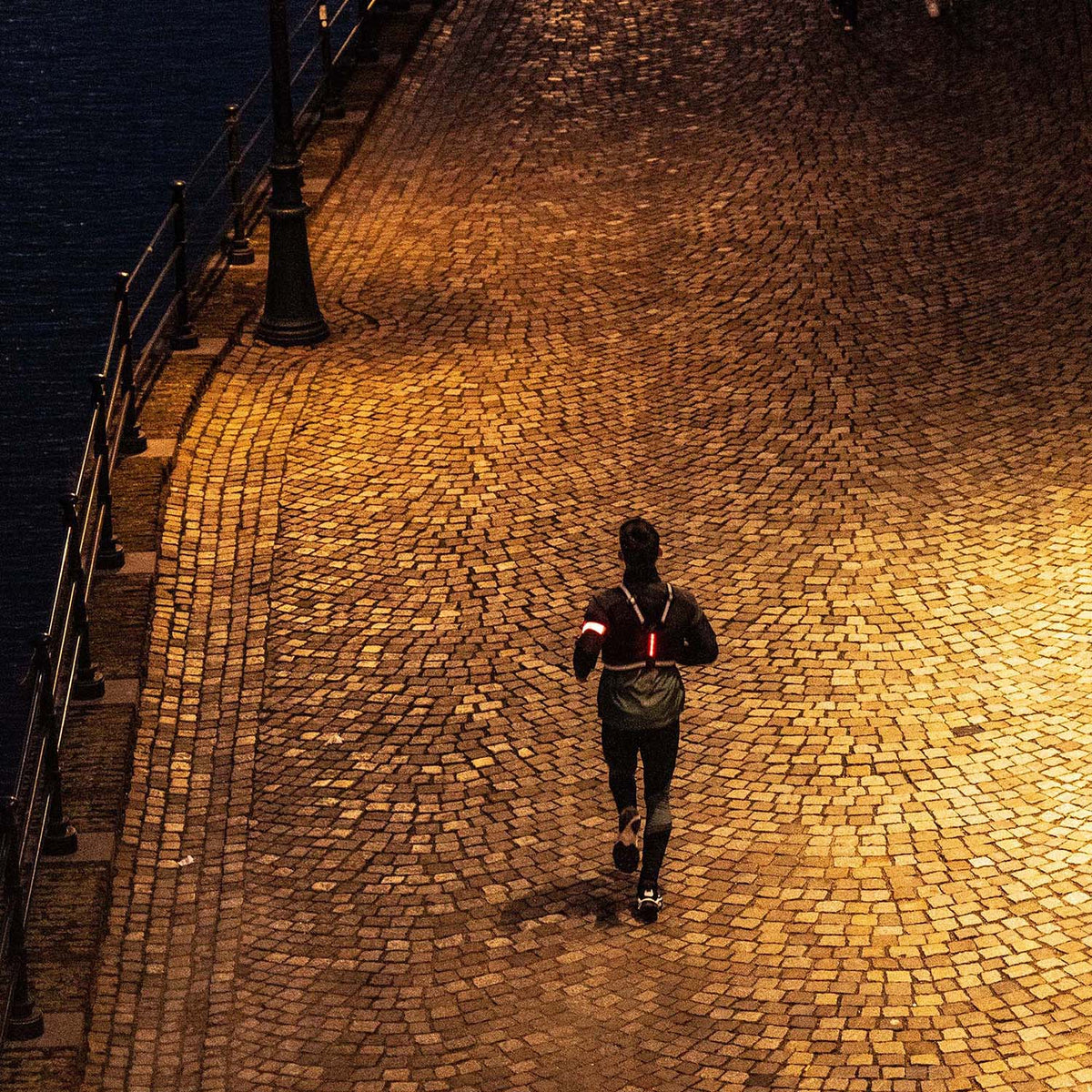 Hardloper in het donker op een verlichte kade met straatverlichting, gezien van bovenaf.