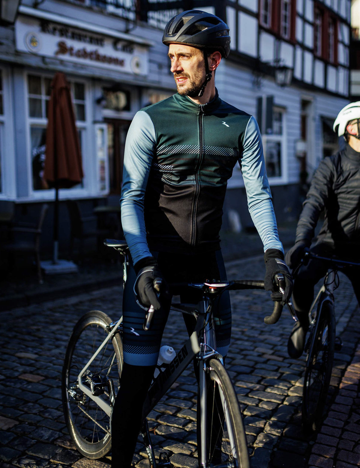 Man in Rogelli Stryde winter fietsjack heren in zwart, grijs en blauw op de racefiets in een stedelijke omgeving.