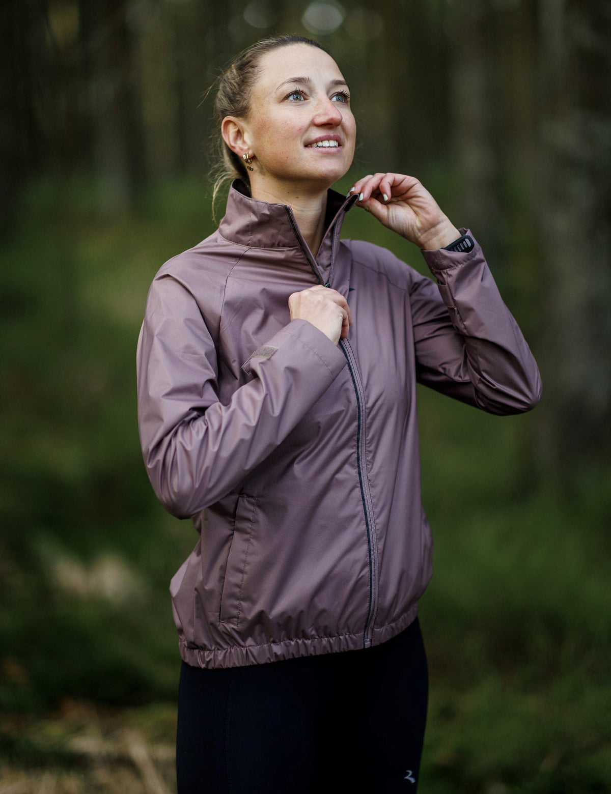 Vrouw in mokkakleurig Rogelli Essential hardloopjack dames voor bescherming tijdens het hardlopen in koel weer.
