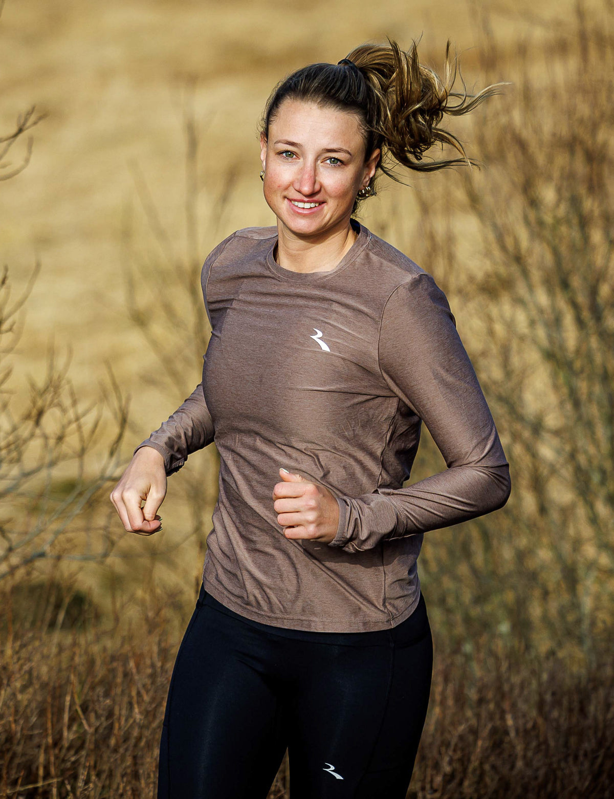Vrouw in mokkakleurig Rogelli Essential hardloopshirt dames met lange mouwen tijdens het hardlopen in de buitenlucht.