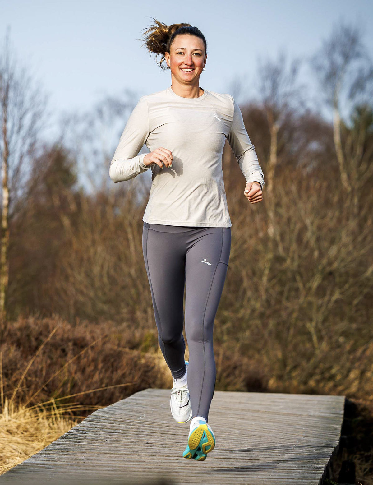 Vrouw in zandkleurig Rogelli Essential hardloopshirt dames met lange mouwen tijdens het hardlopen in de buitenlucht.