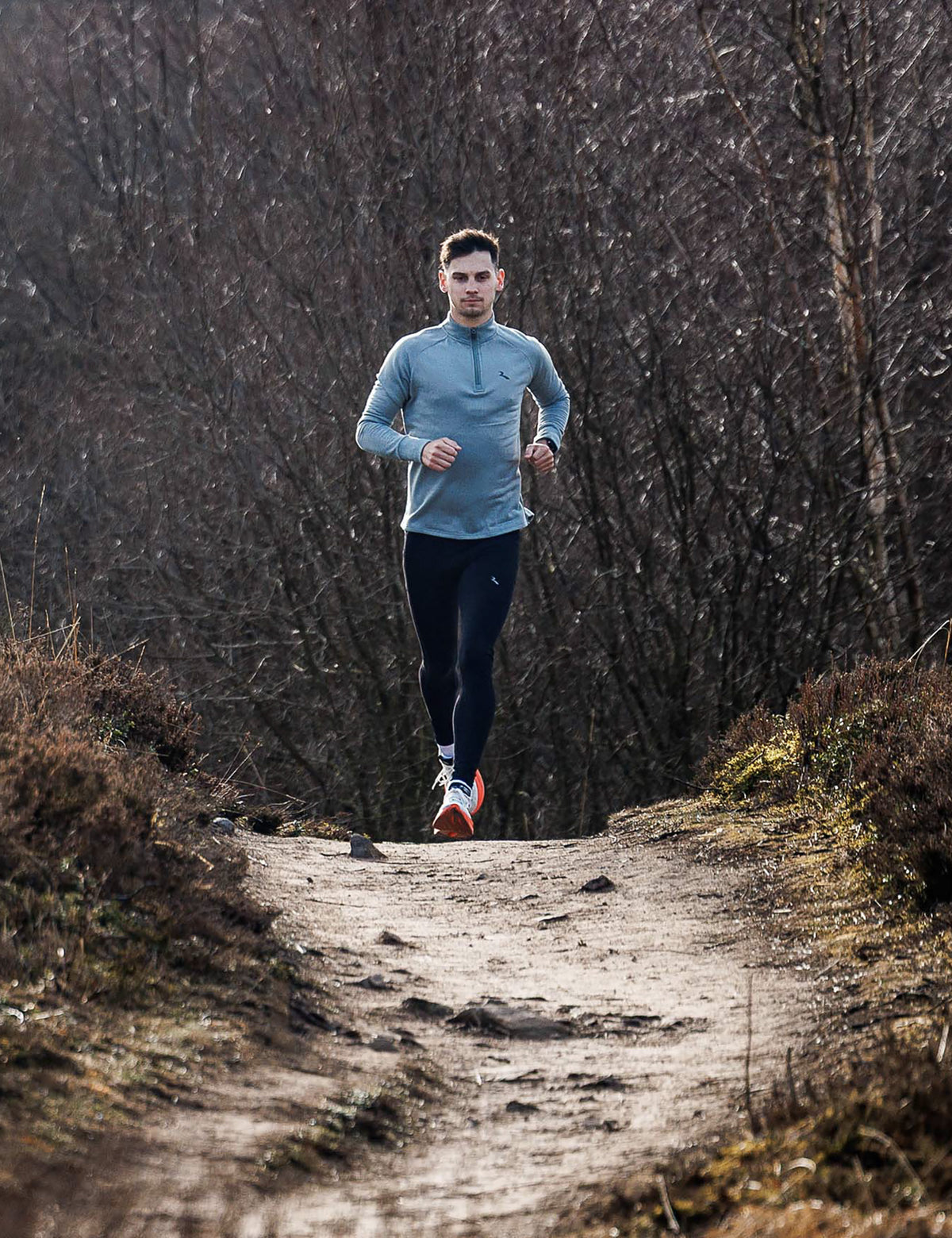 Man in slate Rogelli Essential halfzip hardlooptop heren tijdens het hardlopen op een bospad.