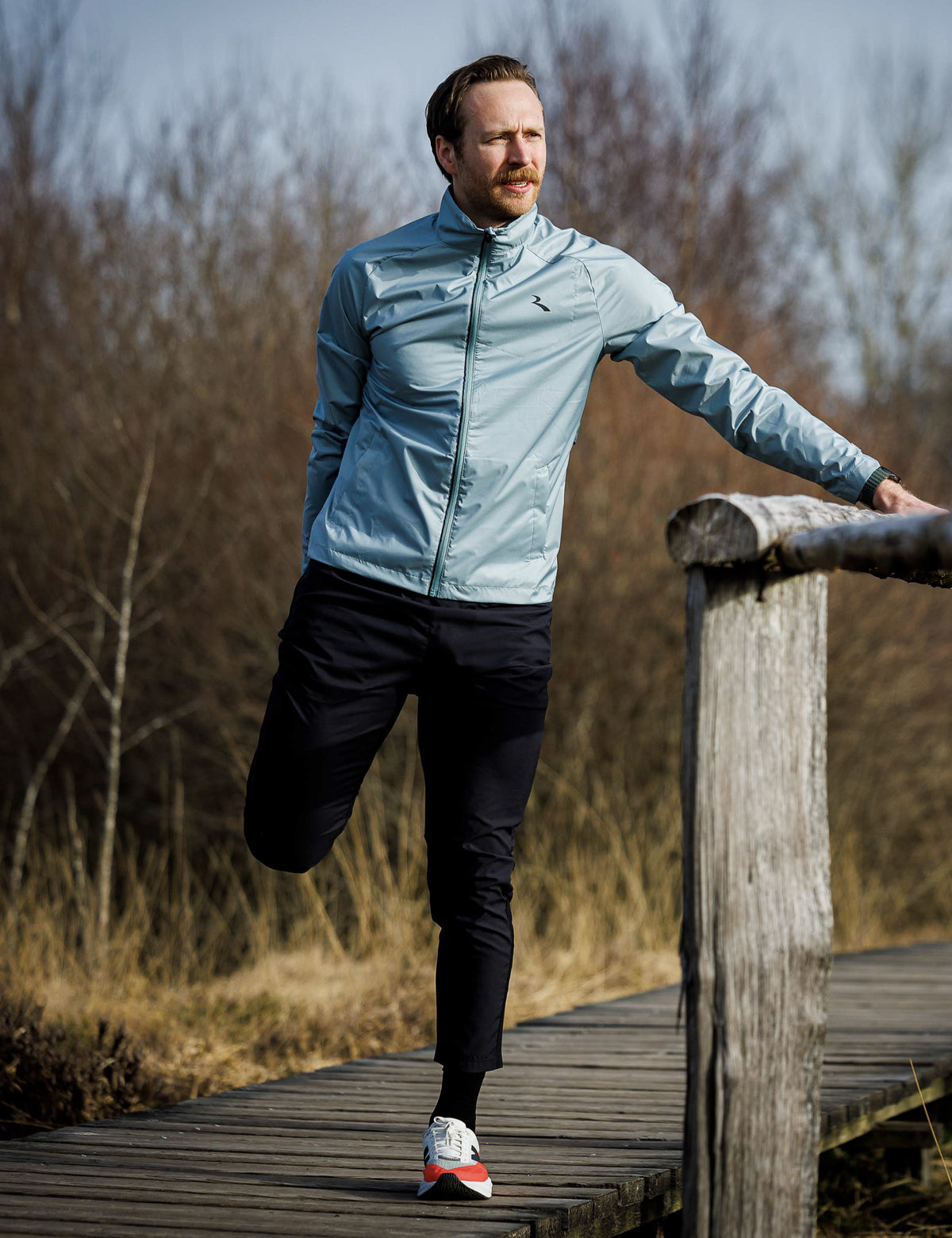 Man in slate Rogelli Essential hardloopjack heren tijdens het rekken voor een hardloopsessie in de buitenlucht.