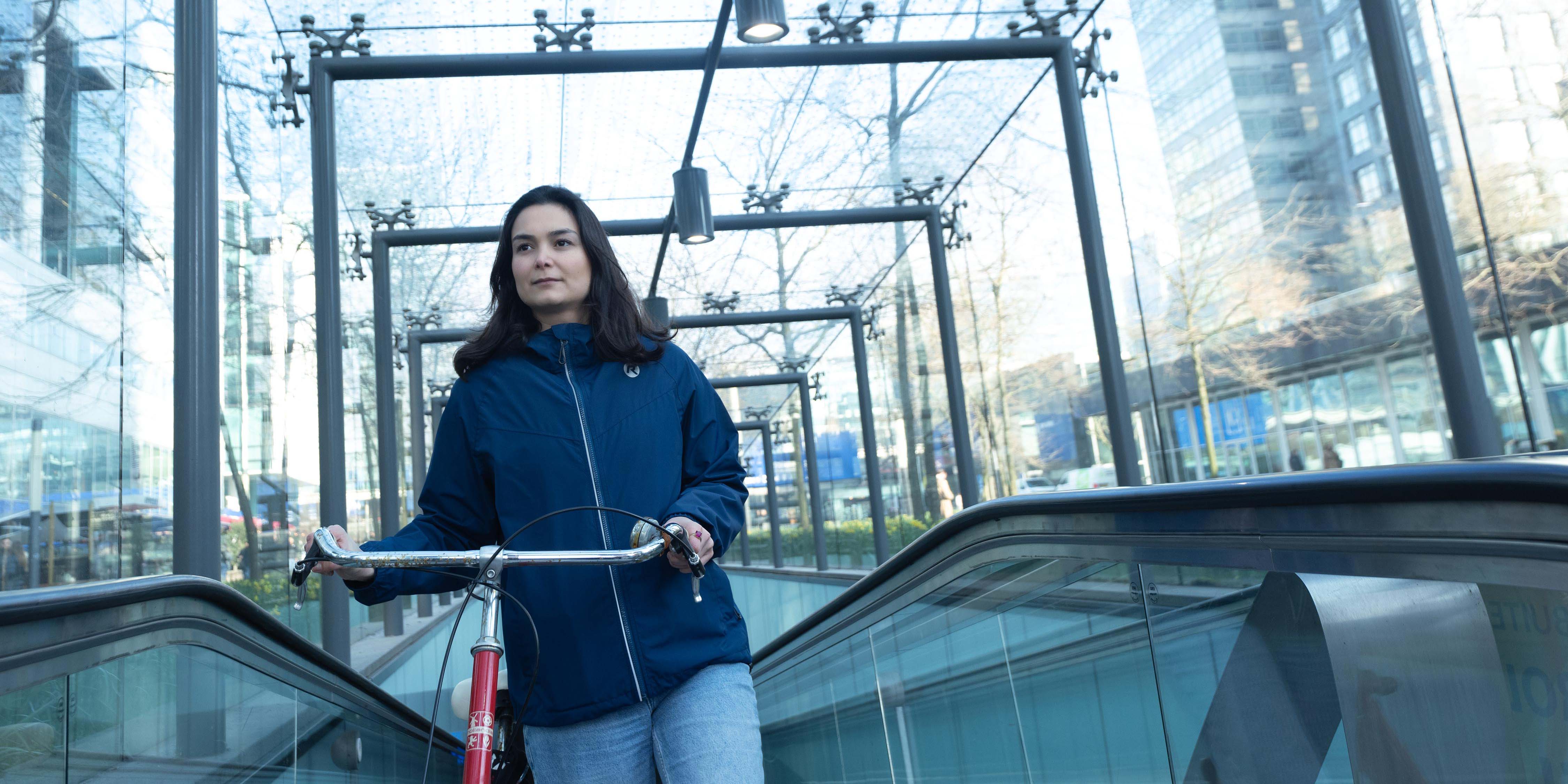 vrouw met fiets in blauwe regenkleding voor woon-werk verkeer.