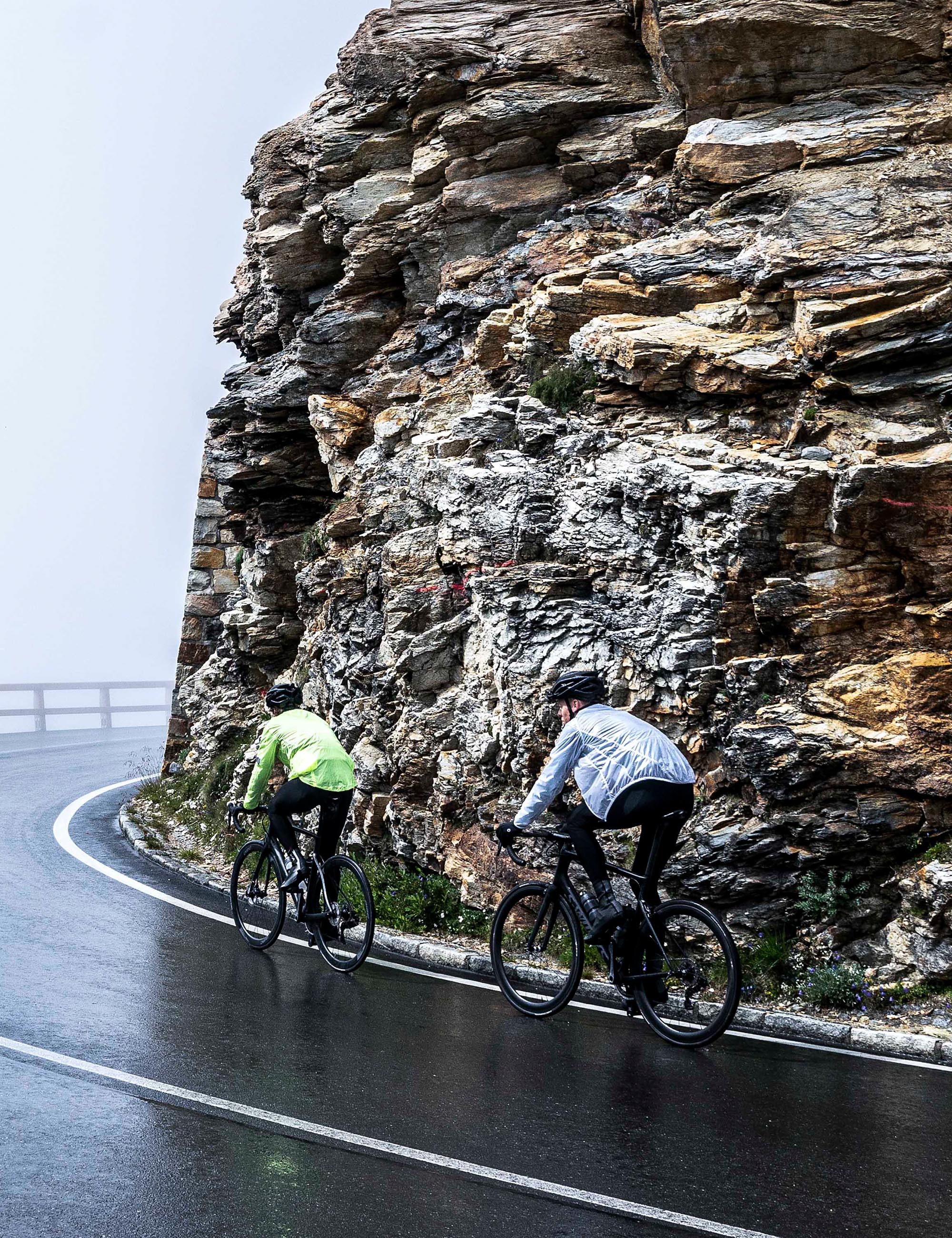 Een mannelijke en vrouwelijke wielrenner fietsen in de regen met Rogelli Emergency regenjack.