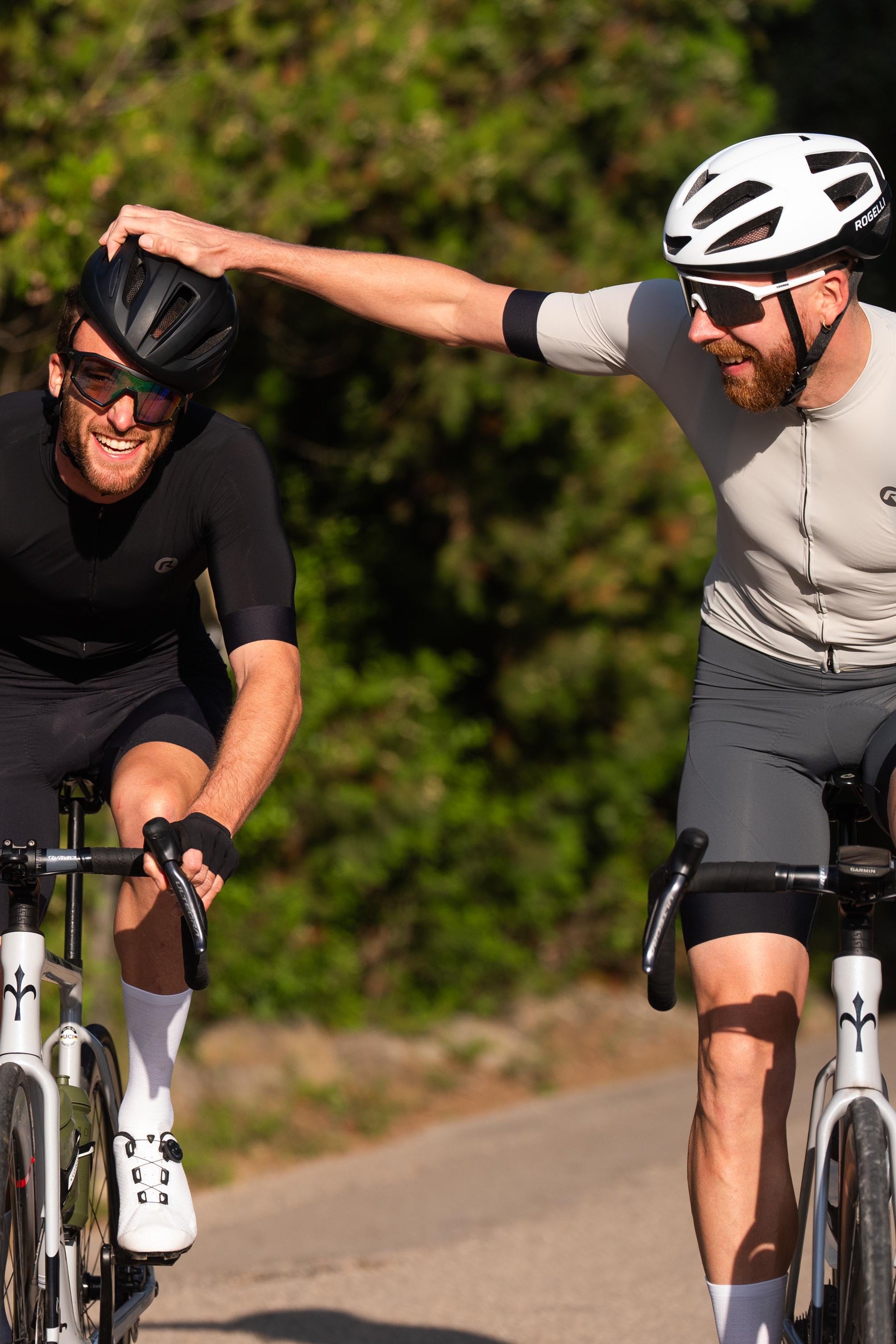 Foto van twee lachende fietsers die aan elkaars helm trekken.