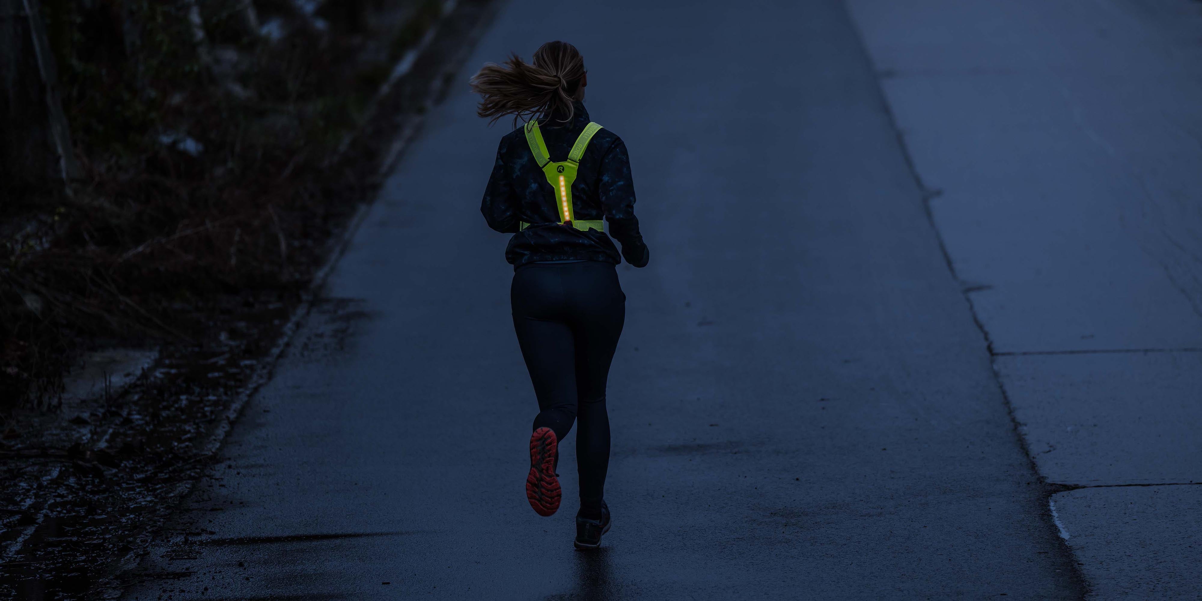 Vrouw met Rogelli hardloopaccessoires dames en reflecterend hardloopvest voor betere zichtbaarheid in het donker.