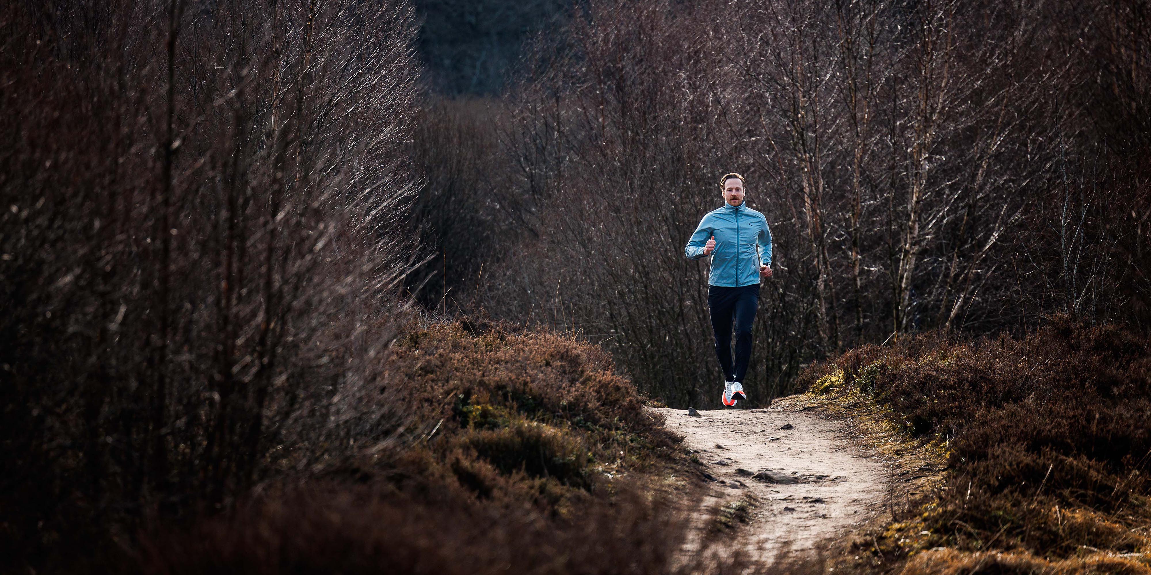 Man in Rogelli hardloopjack heren tijdens het hardlopen op een bospad.