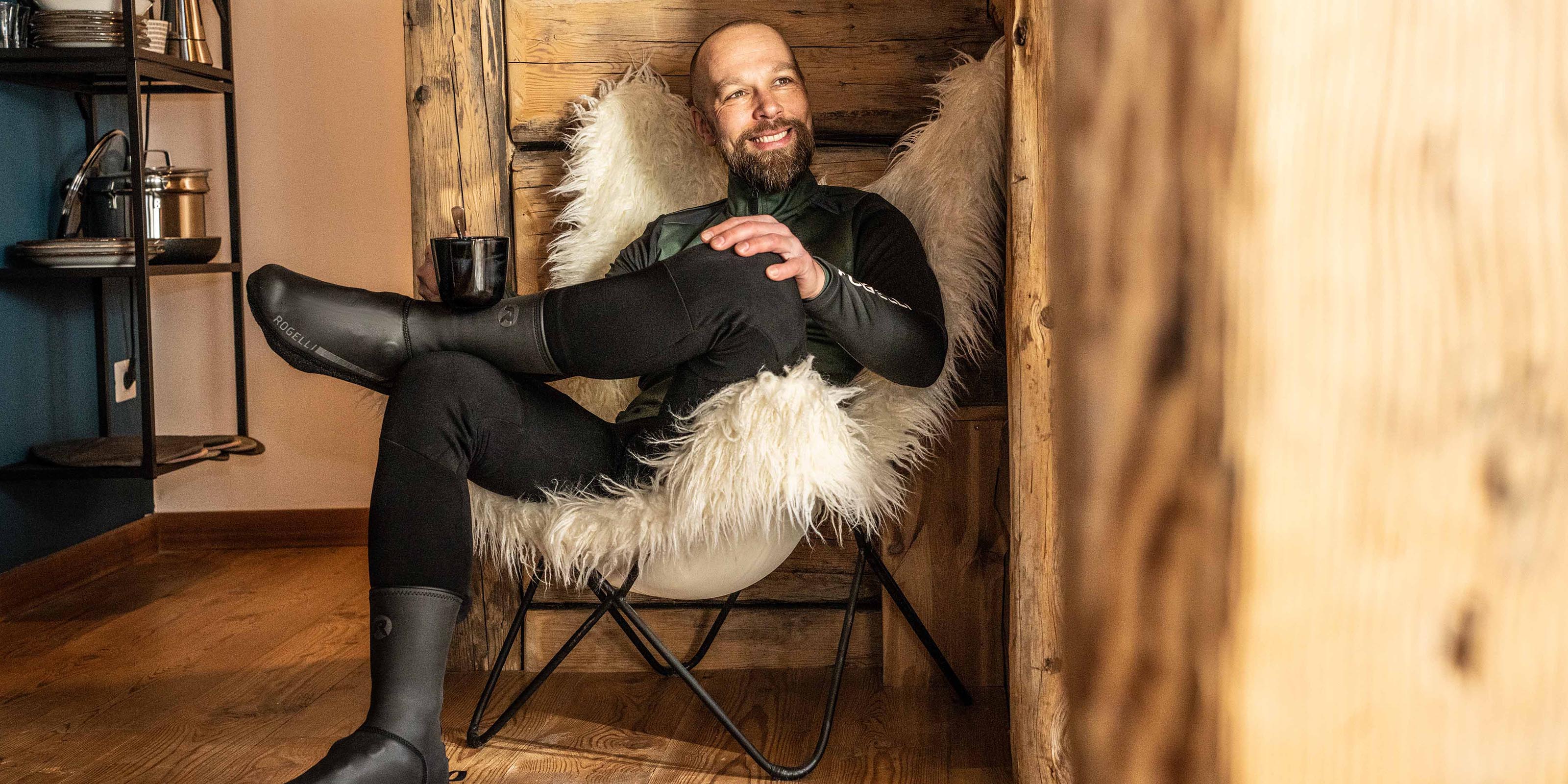 Wielrenner draagt zwarte Rogelli overschoenen en zit binnen op een stoel.