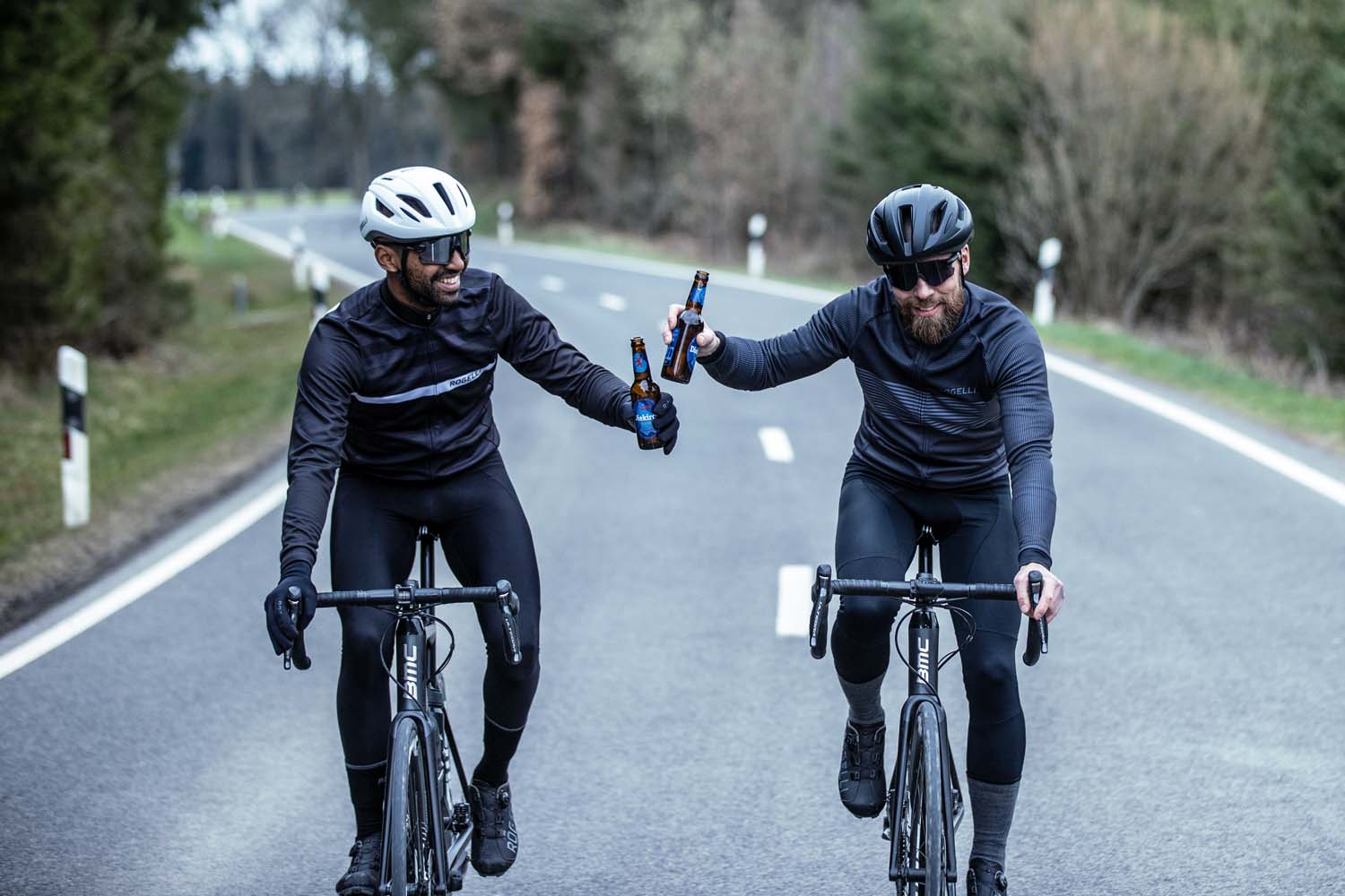 Twee wielrenners proosten op een geslaagde rit terwijl ze genieten van een verfrissend drankje onderweg, omringd door de schoonheid van de natuur.