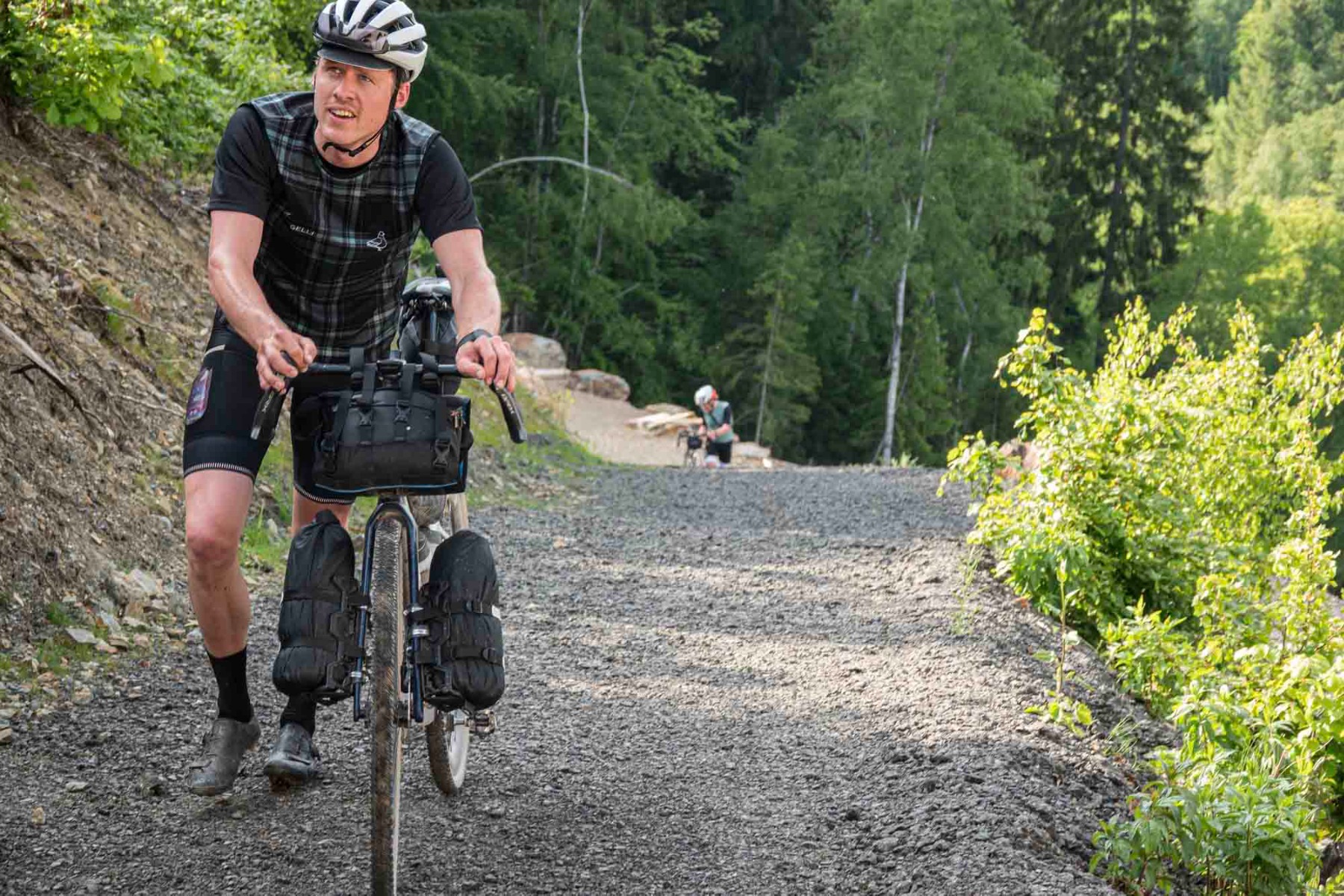 Een fietser loopt met de fiets aan de hand een heuvel op tijdens een bikepacking avontuur, gekleed in Rogelli fietskleding.