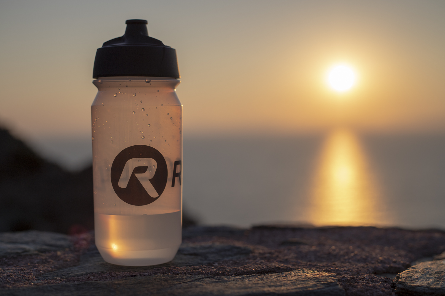 Een Rogelli bidon gevuld met verfrissend water, met een prachtige zonsondergang op de achtergrond.
