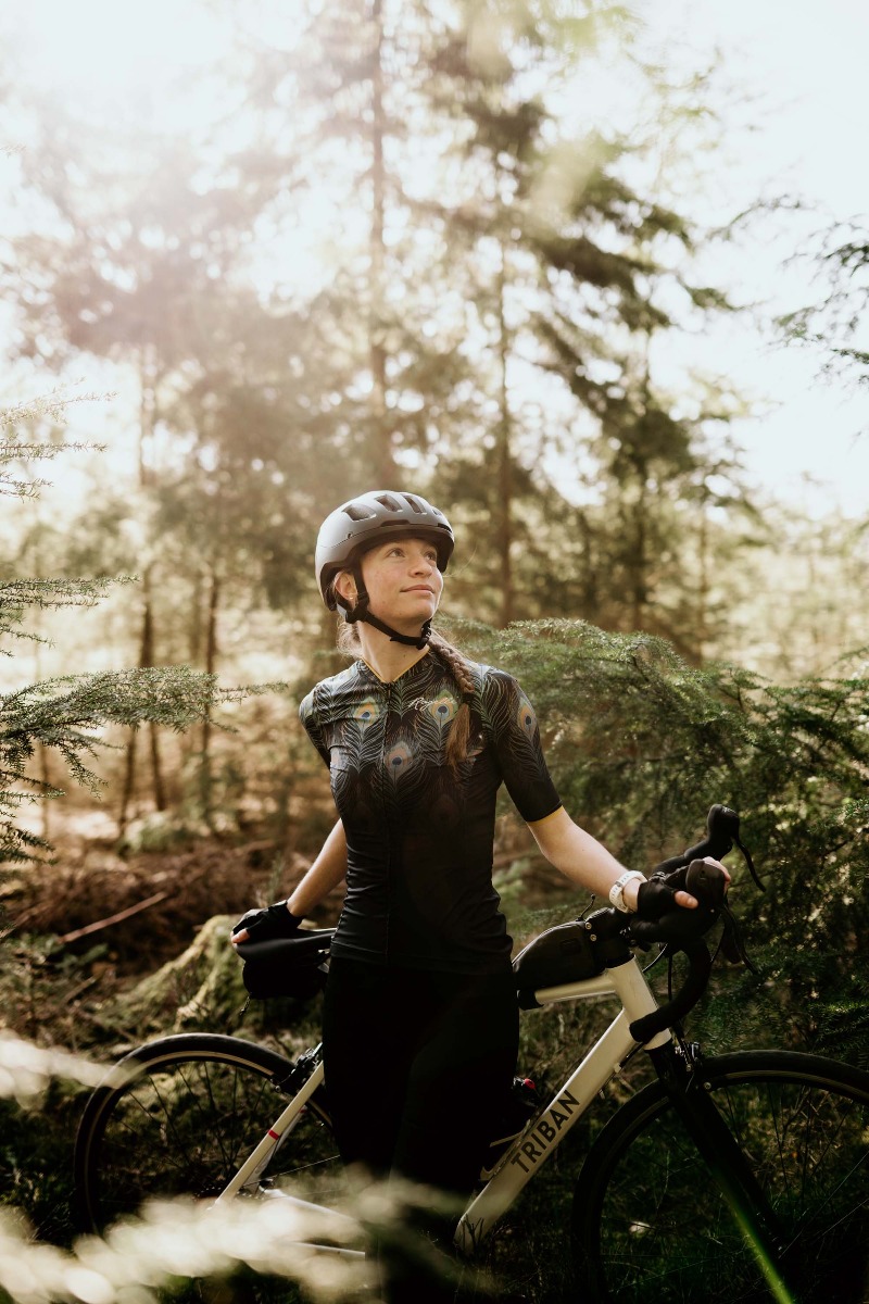 Een vrouwelijke fietser geniet van een ontspannen fietstocht door de bossen, omringd door de rustige schoonheid van de natuur, gekleed in Rogelli fietskleding.