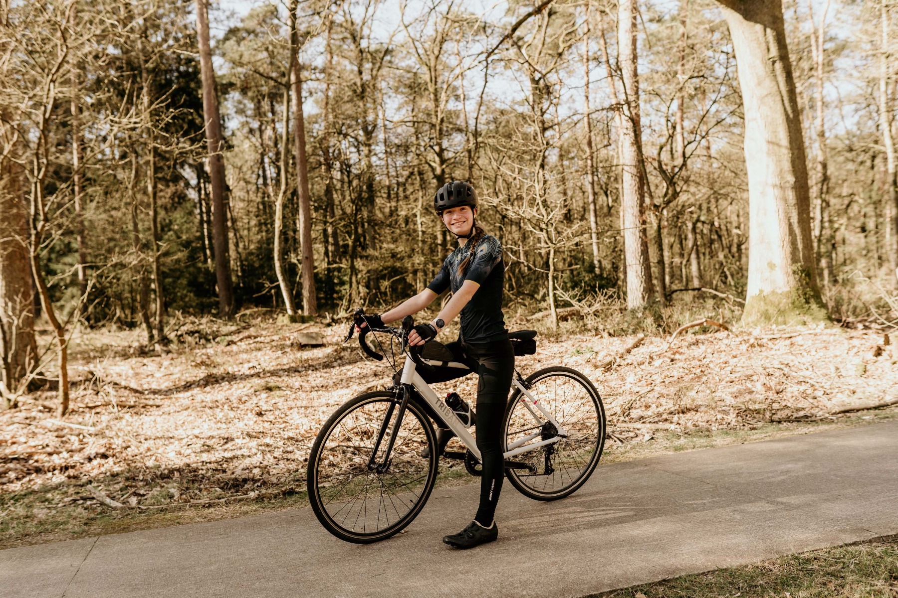 Een vrouwelijke fietser straalt terwijl ze door de bossen fietst, gekleed in Rogelli fietskleding die comfort en stijl combineert voor een plezierige rit.