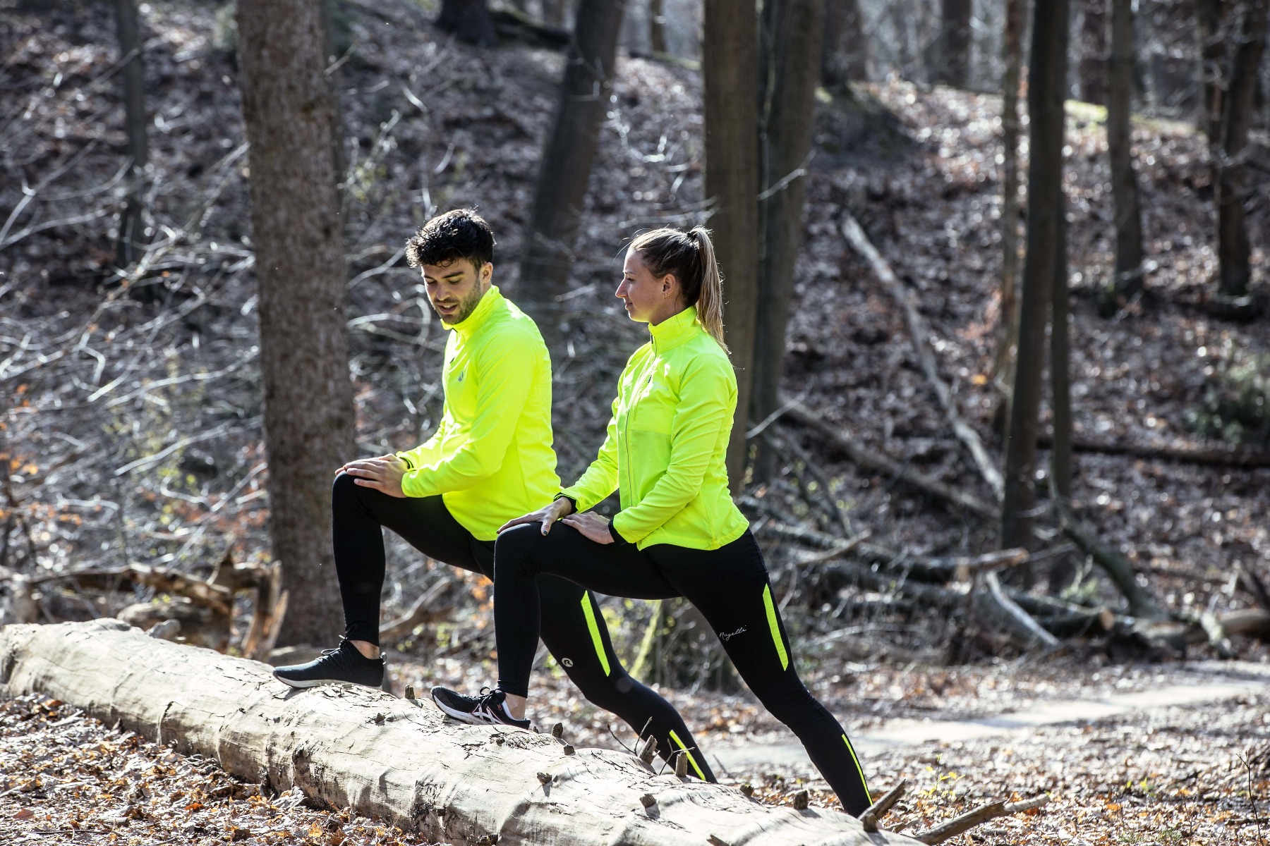 Een man en vrouw voeren rekoefeningen uit voor hun hardloopsessie, gekleed in hoogwaardige Rogelli hardloopkleding voor ultiem comfort en prestaties.