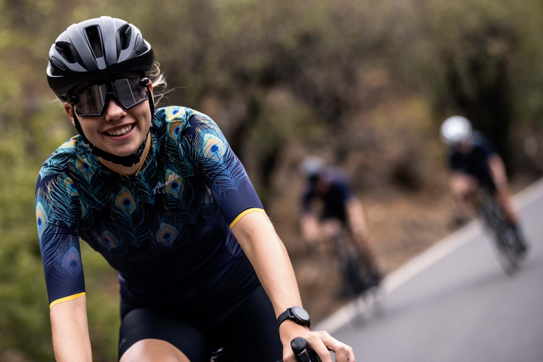 Een afbeelding van een vrouwelijke fietser met een grote glimlach op haar gezicht tijdens het wielrennen, gekleed in een Rogelli fietshelm voor optimale veiligheid en stijl op de weg.