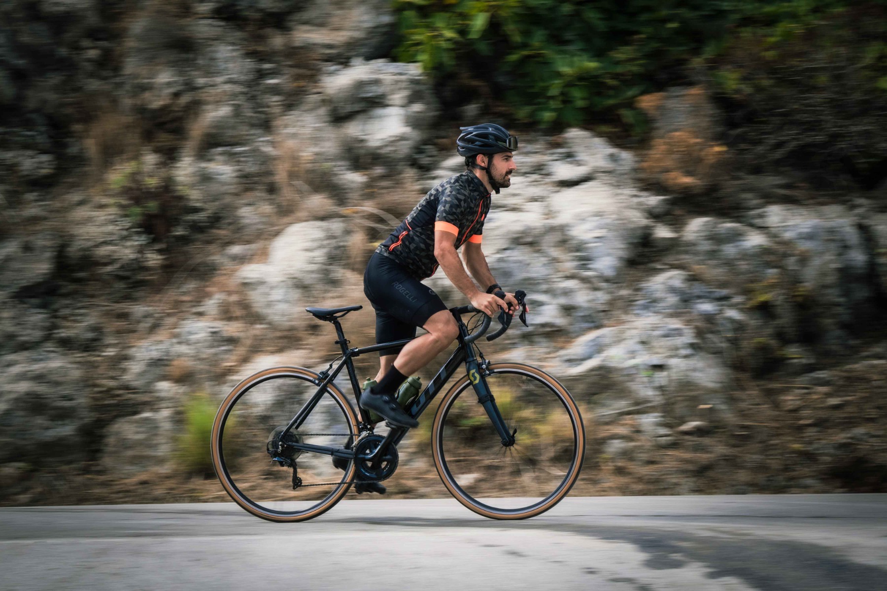 Een wielrenner staat op de pedalen terwijl hij een heuvel beklimt, vastberadenheid en kracht uitstralend tijdens zijn rit met Rogelli fietskleding.