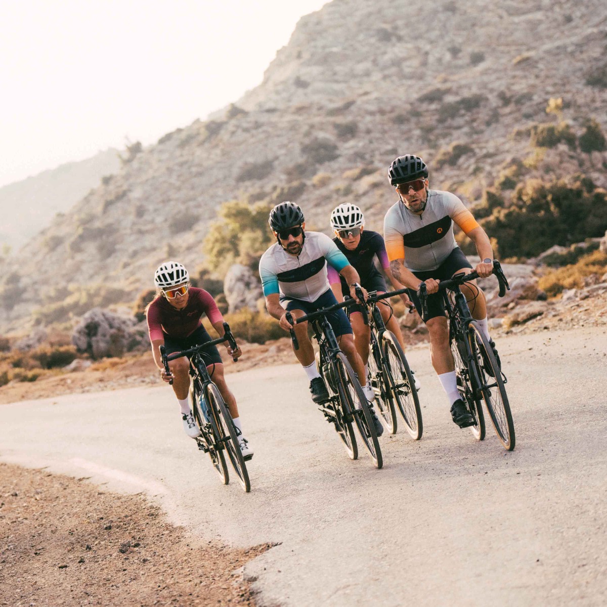 Drie fietsers rijden op hun racefietsen langs de kust, omringd door het prachtige landschap, gekleed in Rogelli fietskleding