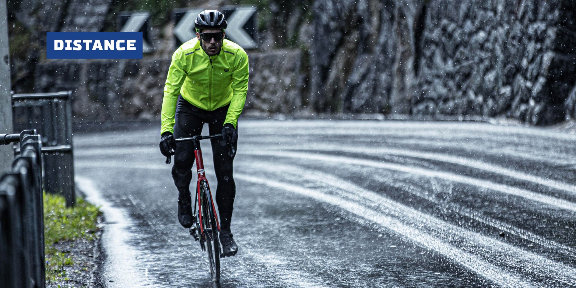 Mannelijke wielrenner in fluoriserend Rogelli regenjack fietsend in een zware regenbui
