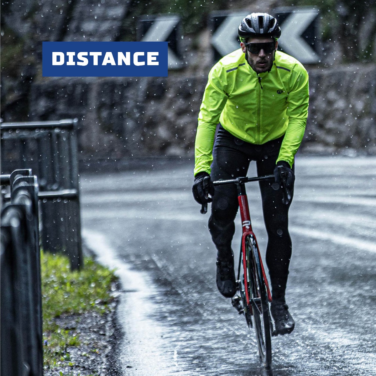 Mannelijke wielrenner in fluoriserend Rogelli regenjack fietsend in een zware regenbui