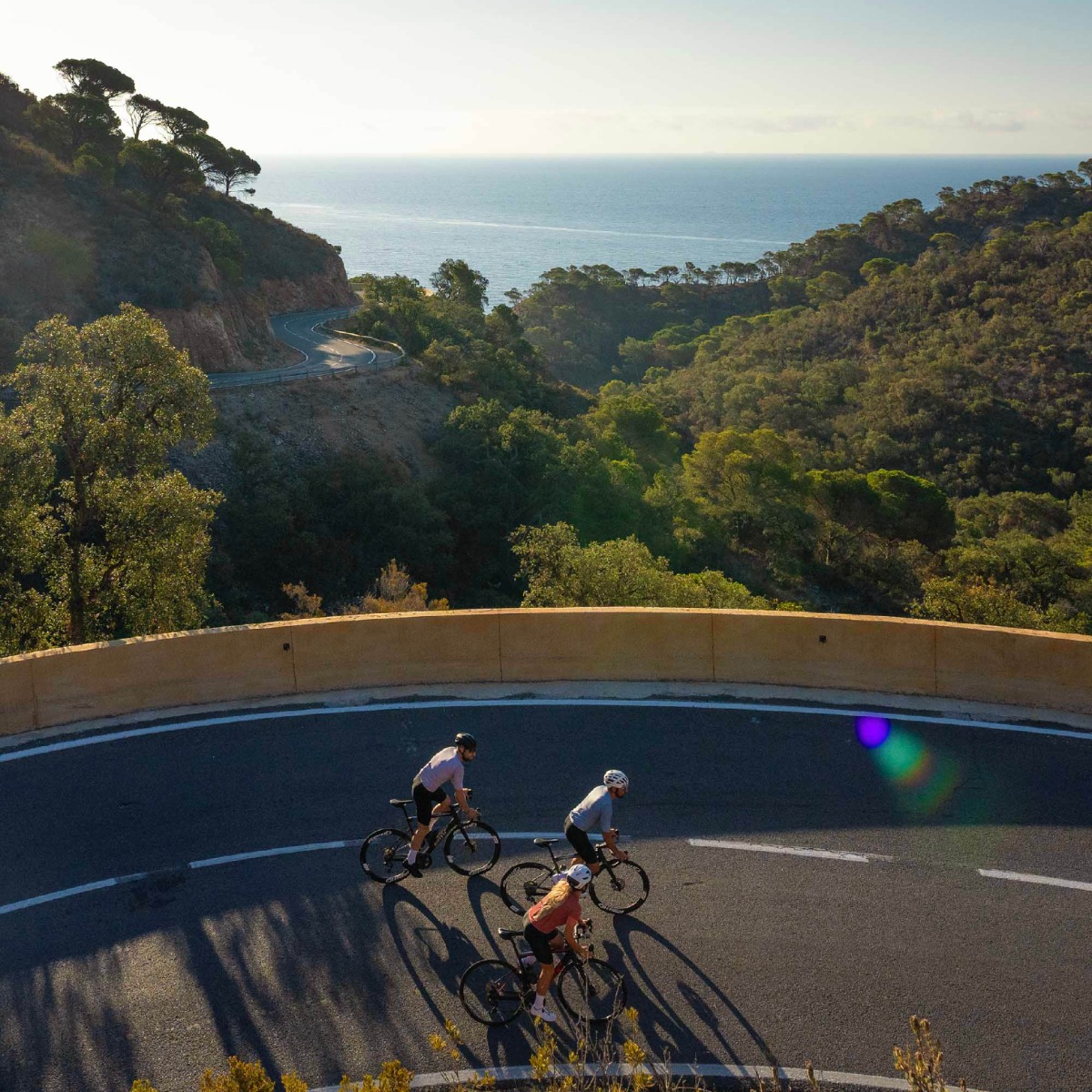 Twee fietsers beklimmen een steile helling met de glinsterende Middellandse Zee op de achtergrond, omringd door de adembenemende schoonheid van de Costa Brava.