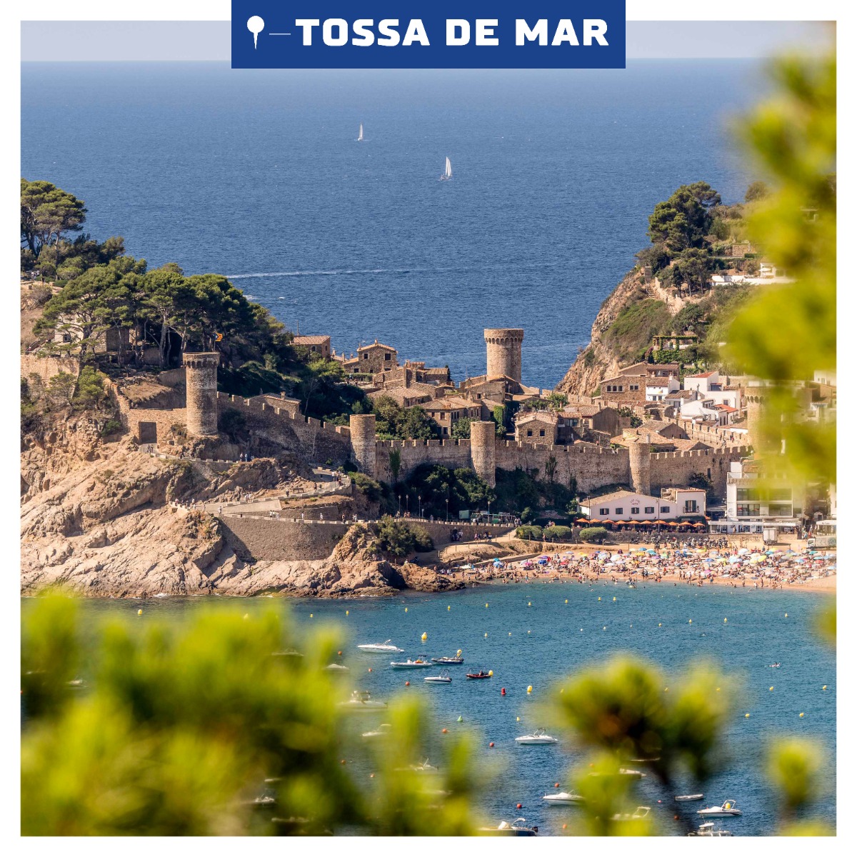 A panoramic photo of Tossa de Mar, seen from a distance, with the medieval city walls standing atop a hill surrounded by the azure waters of the Mediterranean Sea.