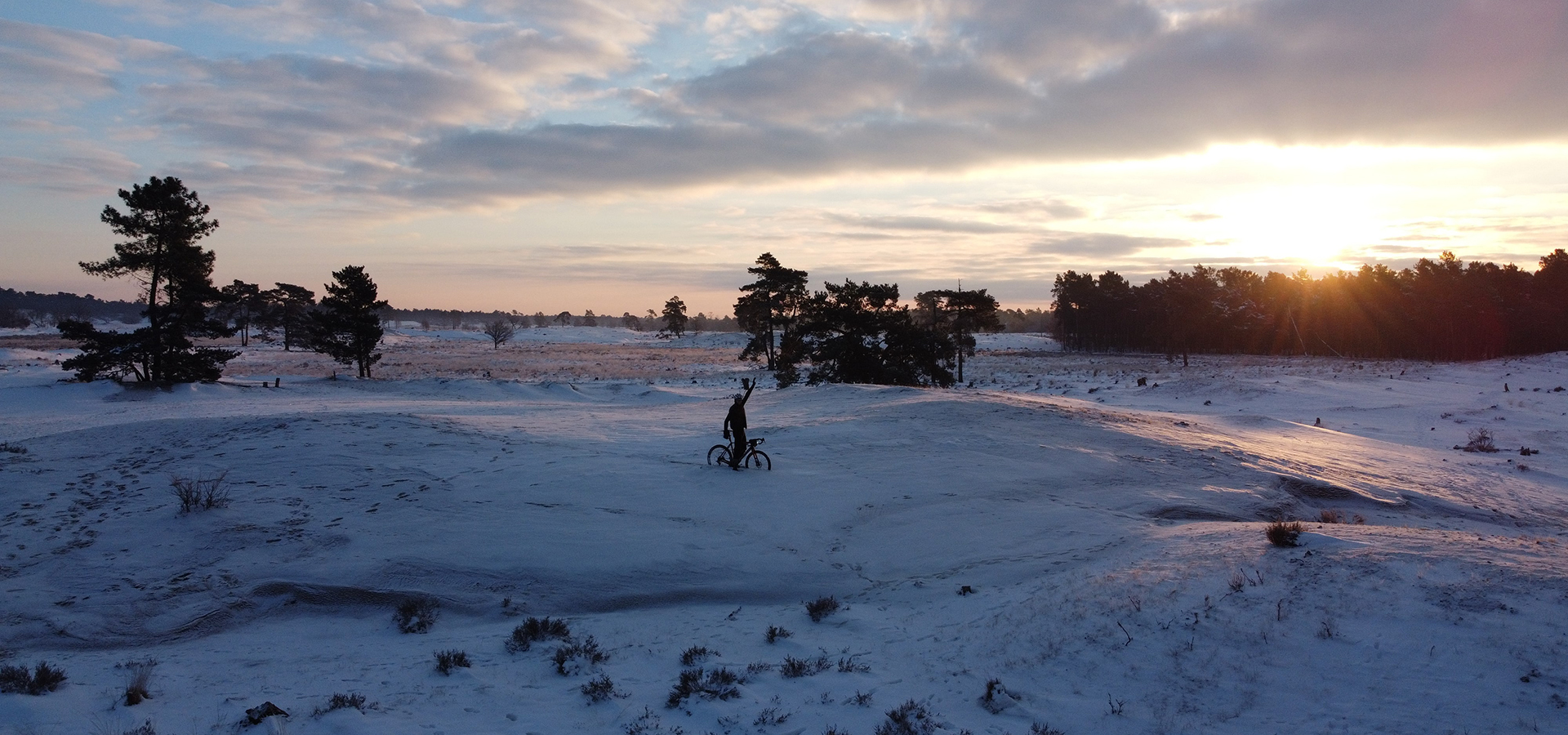 Verken de winterse pracht met Rogelli fietskleding, terwijl een fietser vol trots zijn fiets in de sneeuw presenteert. Voel de warmte en bescherming, zelfs in koude omstandigheden!
