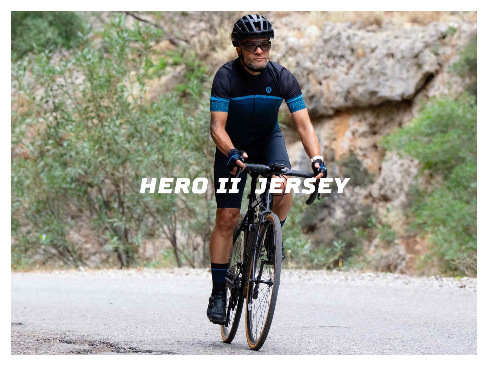 Mannelijke wielrenner fietsend op asfalt tussen de rotsen met het Hero II fietsshirt van Rogelli aan
