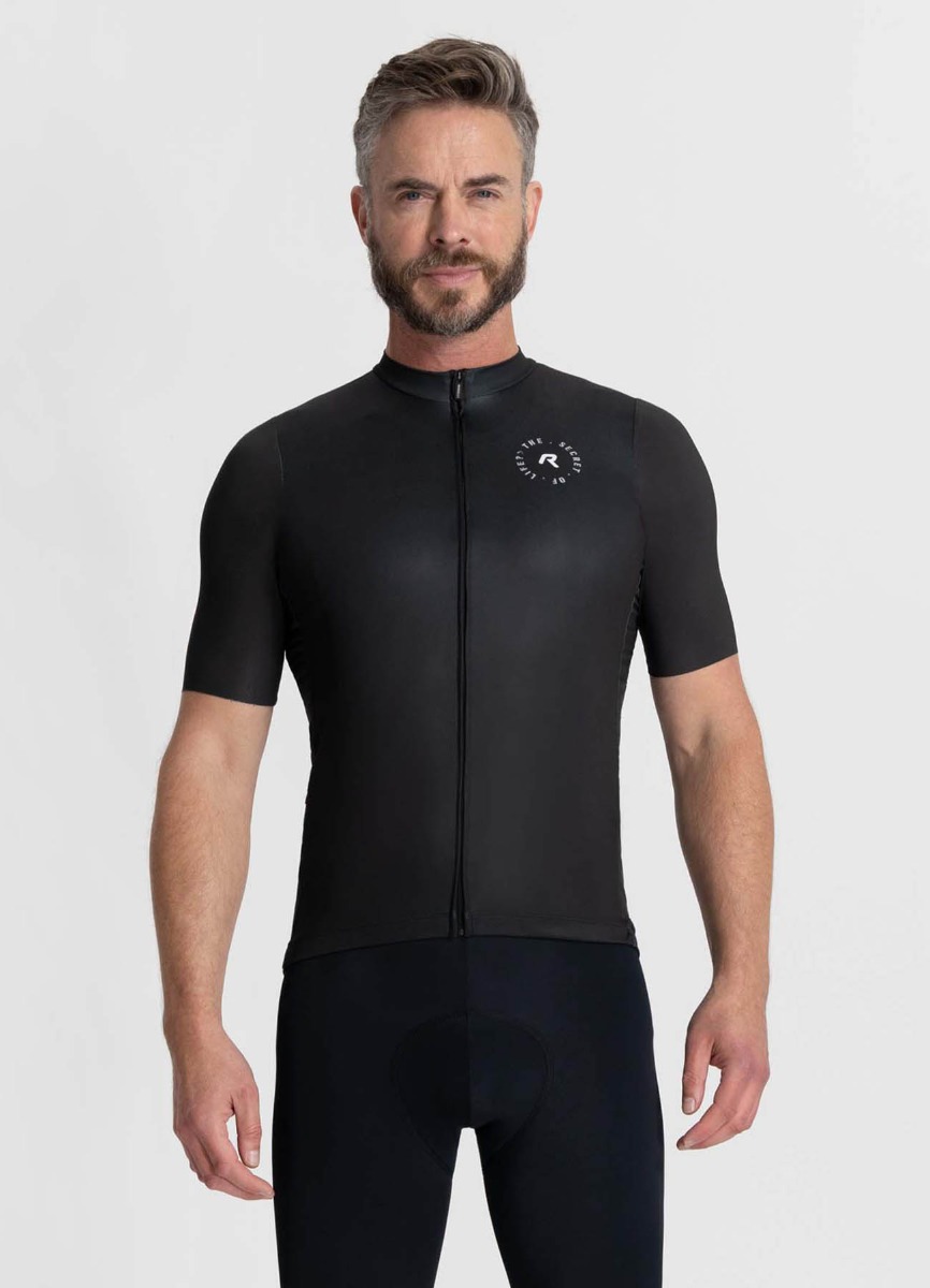 Mannelijk model poserend met het zwarte S.O.L. fietsshirt aan, met grijze achtergrond